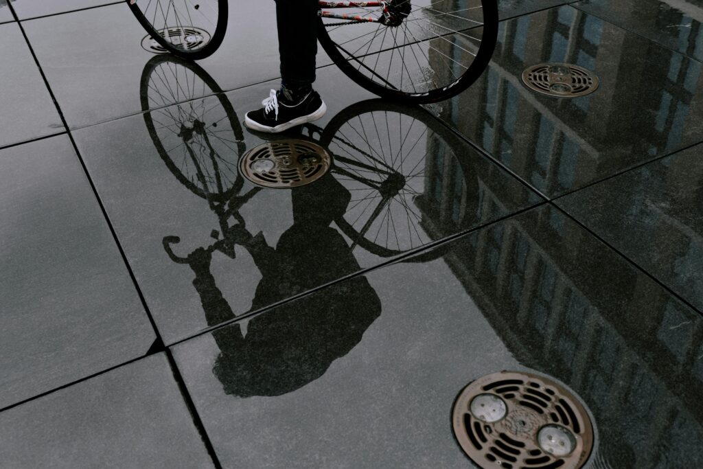 Artistic reflection of a bicycle and person on a wet urban surface, showcasing modern city life.