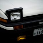 Close-up of a classic white Toyota AE86 Trueno with pop-up headlights.